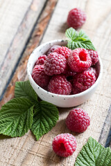 fresh juicy raspberries with green leaves in a plate on a wooden table. Healthy berry, organic food, antioxidant