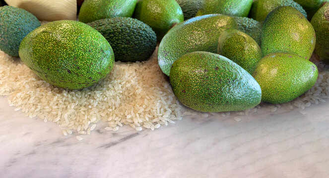 Close-up of rice grains and fresh avocado fruits standing on marble floor