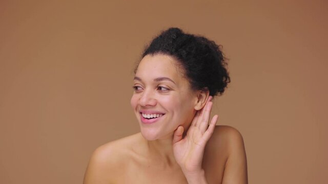 Beauty portrait of young African American woman holding hand near ear trying, listen news and gossip. Black female model posing on brown studio background. Slow motion ready, 4K at 59.94fps.