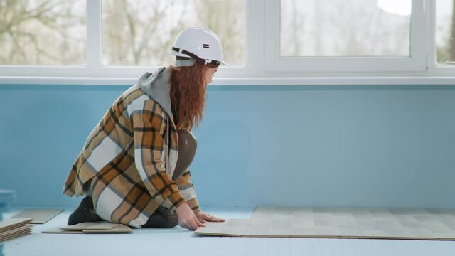 Woman Builder In Helmet Lays Laminate On Floor Insulated With Polyester Foam In Apartment During Renovation