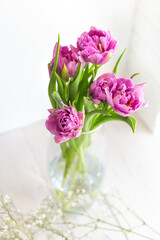 Romantic delicate bouquet of pink tulips in a glass vase on a light background. Greeting card for mother's day, march 8 or wedding. Floristics, flower shop. The freshness of a spring morning.