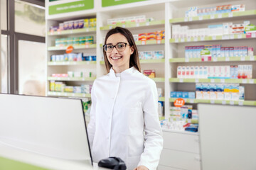 Pharmacist at the counter. A young woman in a white uniform focused on work at the computer is smiling at patients. The woman at work, pharmacist job, professional development