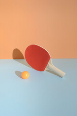 A red ping pong racket on a blue background with a ball in front. Sport table tennis still life concept.