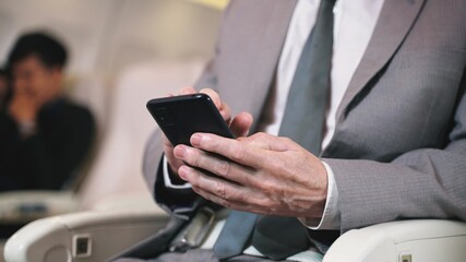 Business man texting in smartphone in airplane. Caucasian businessman using smart phone in first class section of commercial airliner. Detail view of man's hand with camera dolly movement.