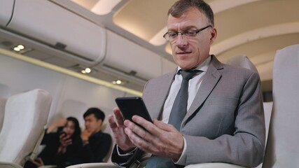 Fototapeta na wymiar Business man texting in smartphone in airplane. Caucasian businessman using smart phone in first class section of commercial airliner. Detail view of man's hand with camera dolly movement.