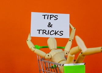 Tips and tricks symbol. White paper. Words 'Tips and tricks'. Miniature shopcart, wooden human. Beautiful orange background. Business and tips and tricks concept, copy space.