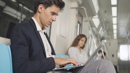 Businessman using laptop for working in the train and communicates on wireless headphones. Caucasian white male working on laptop while traveling by train.