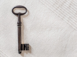 Old iron key on white linen napkin in Provence rustic style, flat lay.