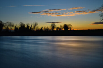 Fototapeta premium incredible sunset on the Muzza river, lights, colors and reflections surround this breathtaking landscape