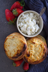 Vatrushka - Traditional Russian open pie with cottage cheese. Top view photo of sweet buns, cottage cheese, blue ceramic cup with milk, juicy strawberries