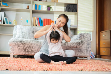 Beautiful young woman and her charming little daughter, doing yoga together at home
