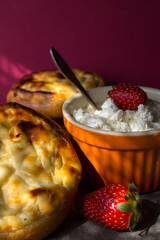 Freshly baked cream-cheese buns and strawberries on pink background. Appetizing pastries with cottage. 
