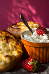 Freshly baked cream-cheese buns and strawberries on pink background. Appetizing pastries with cottage. 
