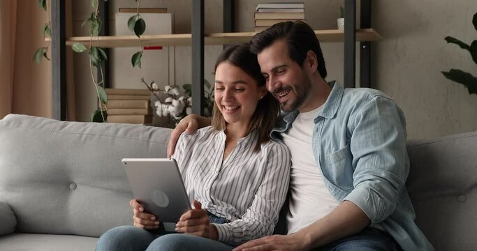 Married couple sit on sofa making video call using internet and digital tablet device. Remote communication, pleasant videoconference conversation with family. Modern technology, apps usage concept