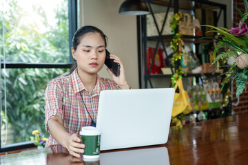 Young charming woman talking to the phone, working on a laptop and drinking coffee in a cafe.  Attractive female calling with her cell telephone. Student learning online. Freelancer working online.