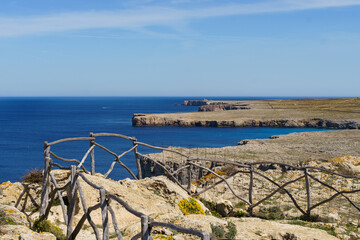 View of Punta Nati lighthouse from Sa Falconera point of view (Menorca, Balearic Islands, Spain) in a sunny day with blue sky