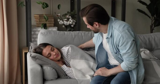 Tired housewife falling asleep on sofa in living room, caring husband cover sleeping beautiful female with warm cozy plaid expressing care, keep about healthy and comfort rest of wife. Cherish concept