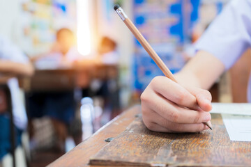 School students hard at work in the classroom sitting with his head on his hand reading and writing notes on sheets