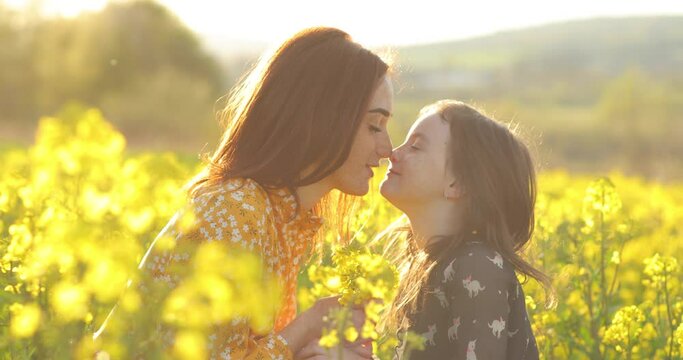A friendly and loving family in nature. Emotional portrait of a happy and cheerful beautiful young mother playing with her little laughing daughter sitting in a field of rapeseed in the sunset light.