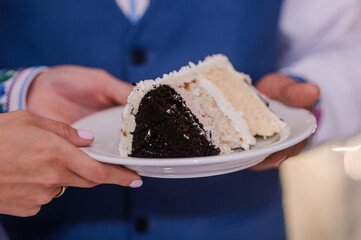 A piece of cake on a white plate in the hands of the bride and groom