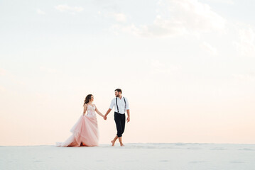 Fototapeta premium young couple a guy in black breeches and a girl in a pink dress are walking along the white sand