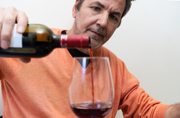 Senior man tasting good cabernet red wine pouring on the wineglass sitting alone on a table, white background