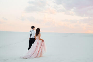 Fototapeta na wymiar young couple a guy in black breeches and a girl in a pink dress are walking along the white sand