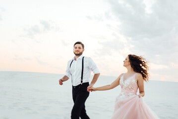 young couple a guy in black breeches and a girl in a pink dress are walking along the white sand
