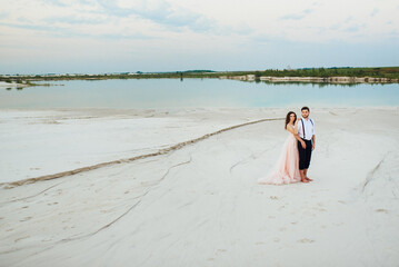 young couple a guy in black breeches and a girl in a pink dress are walking along the white sand