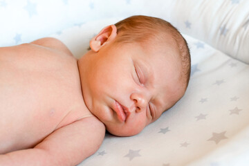 Closeup portrait of Newborn baby sleeping on white blanket. Soft focus. A one weeks old infant is sleeping tightly on her side in bed. 10 days old child.