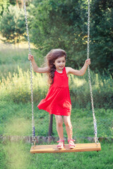 Beautiful little girl is swinging and smiling  in the park at summer day, Happy childhood concept