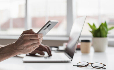 Fototapeta premium Man hands using smart phone and laptop at home closeup, Businessman or student working on computer and texting smartphone at office, Freelance, business, education and technology concept