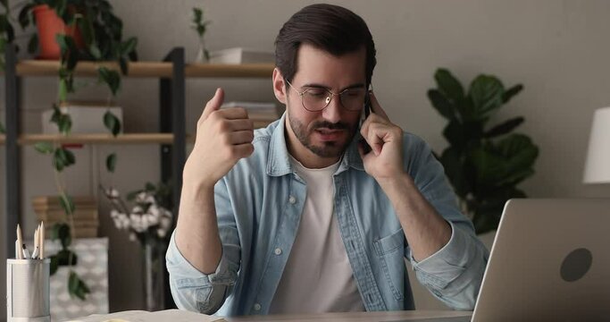 Confident millennial business man sitting at workplace desk talks to client on cell phone, discuss commercial deal with colleague remotely. Mobile operator, roaming, modern technology usage concept