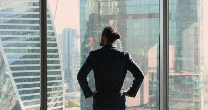 Rearview successful African businessman wear formal suit put hands on waist standing in skyscraper office looks out window to city, plan future project, gets inspiration for business start-up concept
