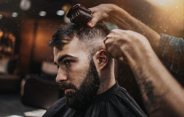 Good looking young adult man getting a hair and beard styling and dressing treatment by...