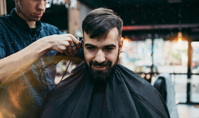 Good looking young adult man getting a hair and beard styling and dressing treatment by professional hairstylist.