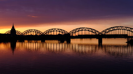 Fototapeta na wymiar Dawn over the Daugava, the sun illuminates the railway bridge in Riga