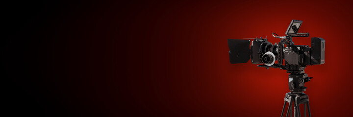 Digital film camera on dark red background, movie production or television banner with copy space
