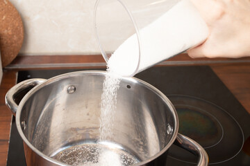 Women's hands pour sugar into a saucepan