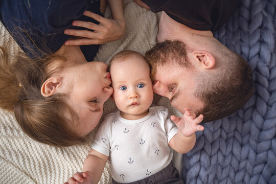 Loving parents, father and mother kiss their beloved child on the cheeks, lying on the bed at home. Happy parenthood. Close-up.
