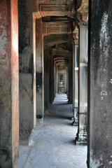 Fototapeta na wymiar Empty corridor inside Angkor Wat complex with crafted Buddha on columns