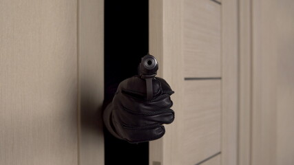 A burglar stands behind the door with a gun aiming at the camera. The bandit opened the door and...