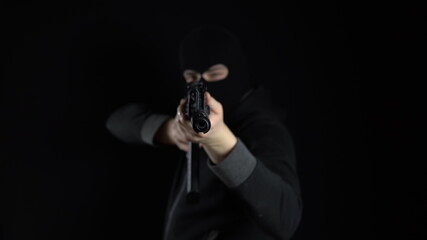A man in a balaclava mask stands with an AK-47 assault rifle. The bandit aims at the camera automatically. On a black background.