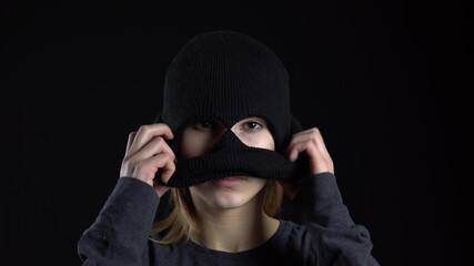 A young woman is putting on a balaclava mask. Bandit on a black background close-up.