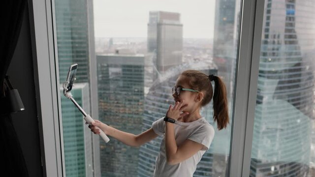 Modern teenage girl taking a selfie near the window in a modern apartment overlooking the city from a high floor. Technology concept, new generation of youth