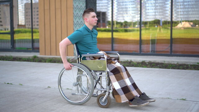 Young man in a wheelchair. A man rides in a wheelchair against the background of a glass building. Special transport for the disabled.