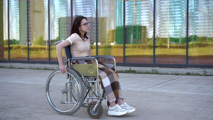 Fototapeta na wymiar Young woman in a wheelchair. A girl rides in a wheelchair against the background of a glass building. Special transport for the disabled.