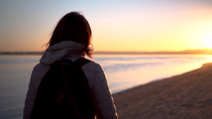 A young woman walks along the beach along the river at sunrise. Silhouette of a girl. Goes to meet the dawn.