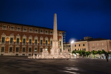 Cityscape. View of Piazza Aranci in Massa with the commemorative monument in the center and on the background the Ducal Palace at night illumination in Massa Tuscany Italy