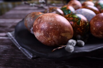 Naturally painted Easter eggs in a black clay plate on a rustic wooden background. Easter eggs painted with onion skins